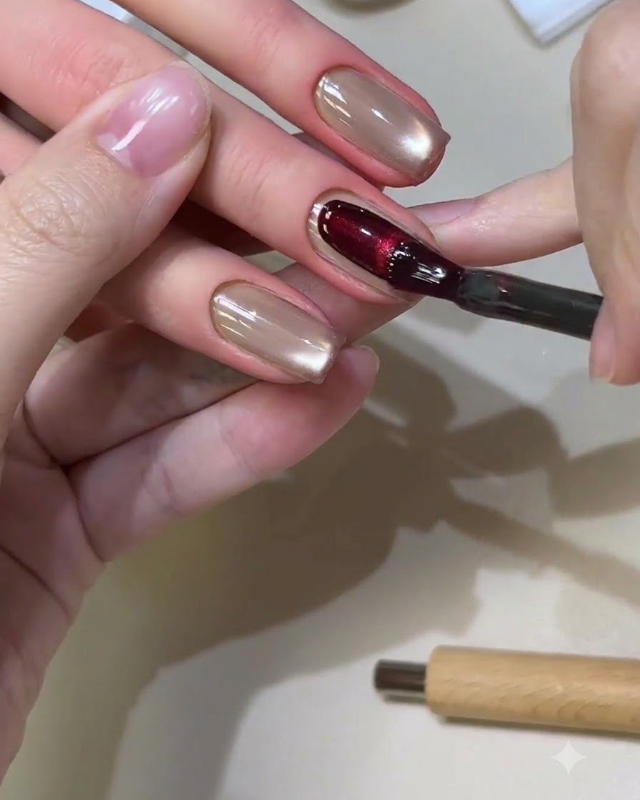 Un pennello per unghie che applica un ricco gel cat-eye rosso su ununghia di forma quadrata.