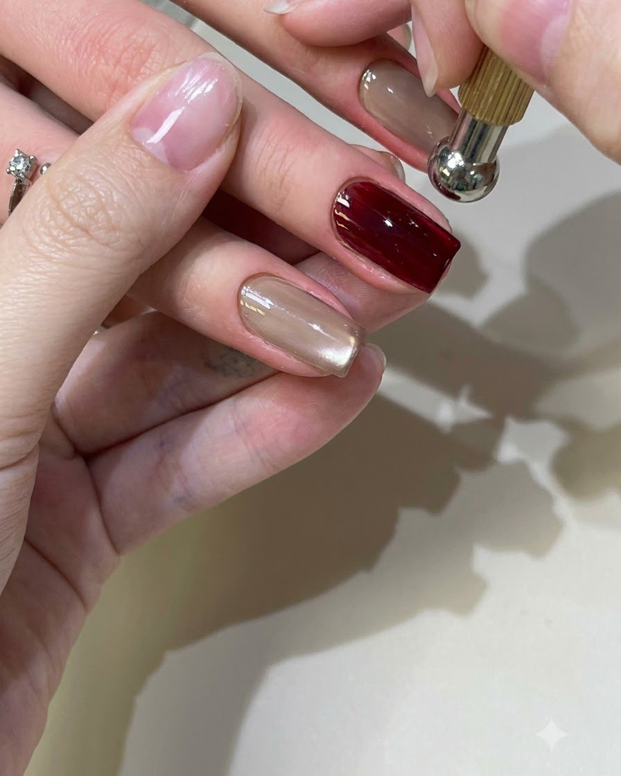 Uno strumento magnetico sferico sospeso sopra ununghia in gel cat-eye rosso per modellare il riflesso della luce.