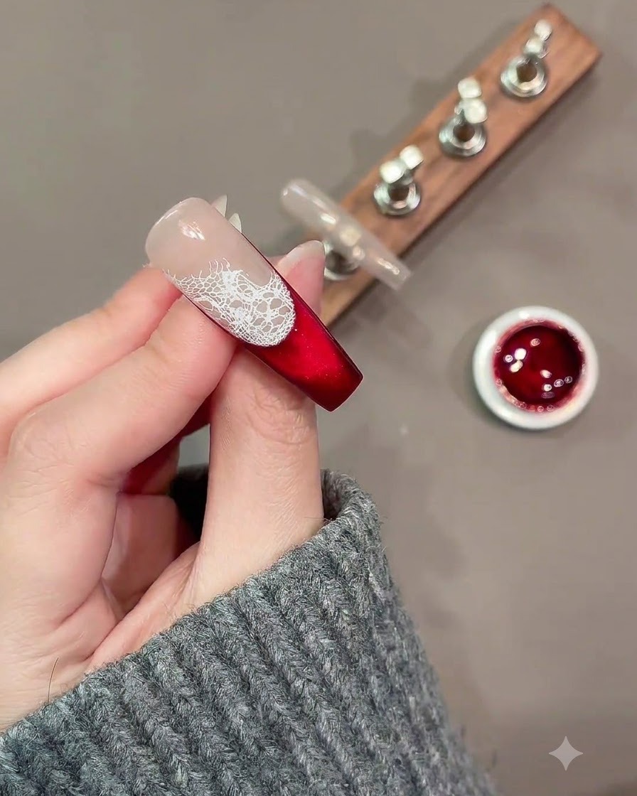 Un pennello fine per nail art dipinge contorni sfusi di rose bianche sopra un motivo in pizzo su ununghia rossa e nude.