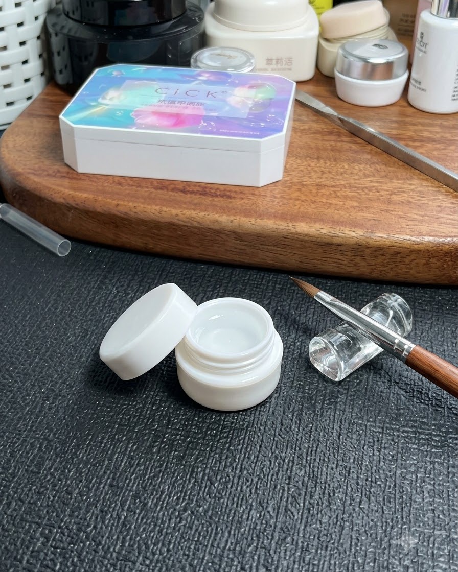 Un barattolo di gel base trasparente posizionato su un tavolo accanto a un pennello fine per nail art e una scatola portaoggetti cosmetica.