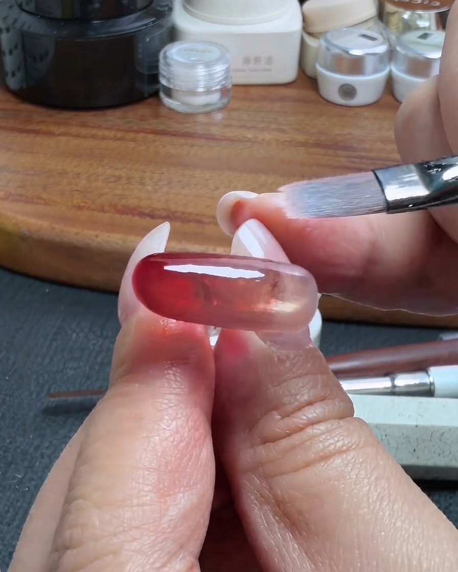 Un pennello da trucco pulito che sfuma delicatamente il bordo di uno strato di gel traslucido rosso su ununghia.