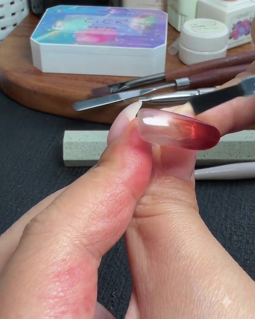 Un pennello che applica un top coat lucido sullunghia completata con gradiente cat-eye rosso e polvere.