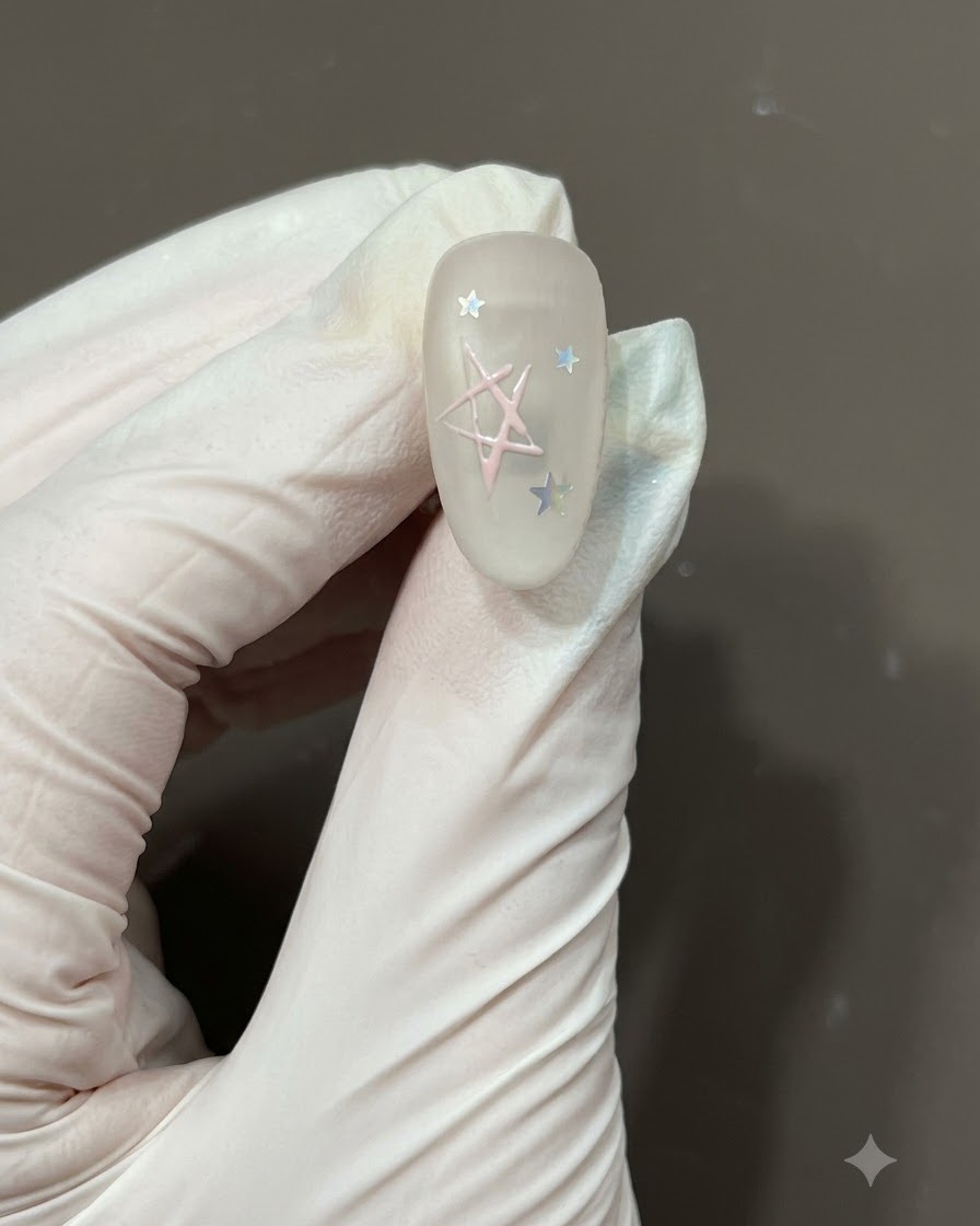 Un pennello per nail art fine che riempie il centro del contorno di una stella disegnata a mano con smalto in gel rosa chiaro su ununghia opaca.