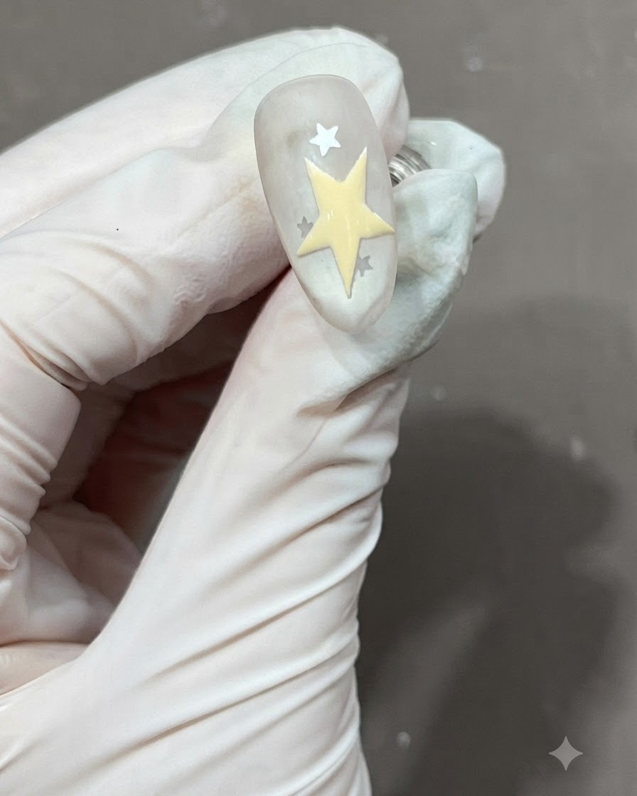 Una stella a cinque punte gialla appena disegnata e riempita accanto ad altre stelle su ununghia opaca.