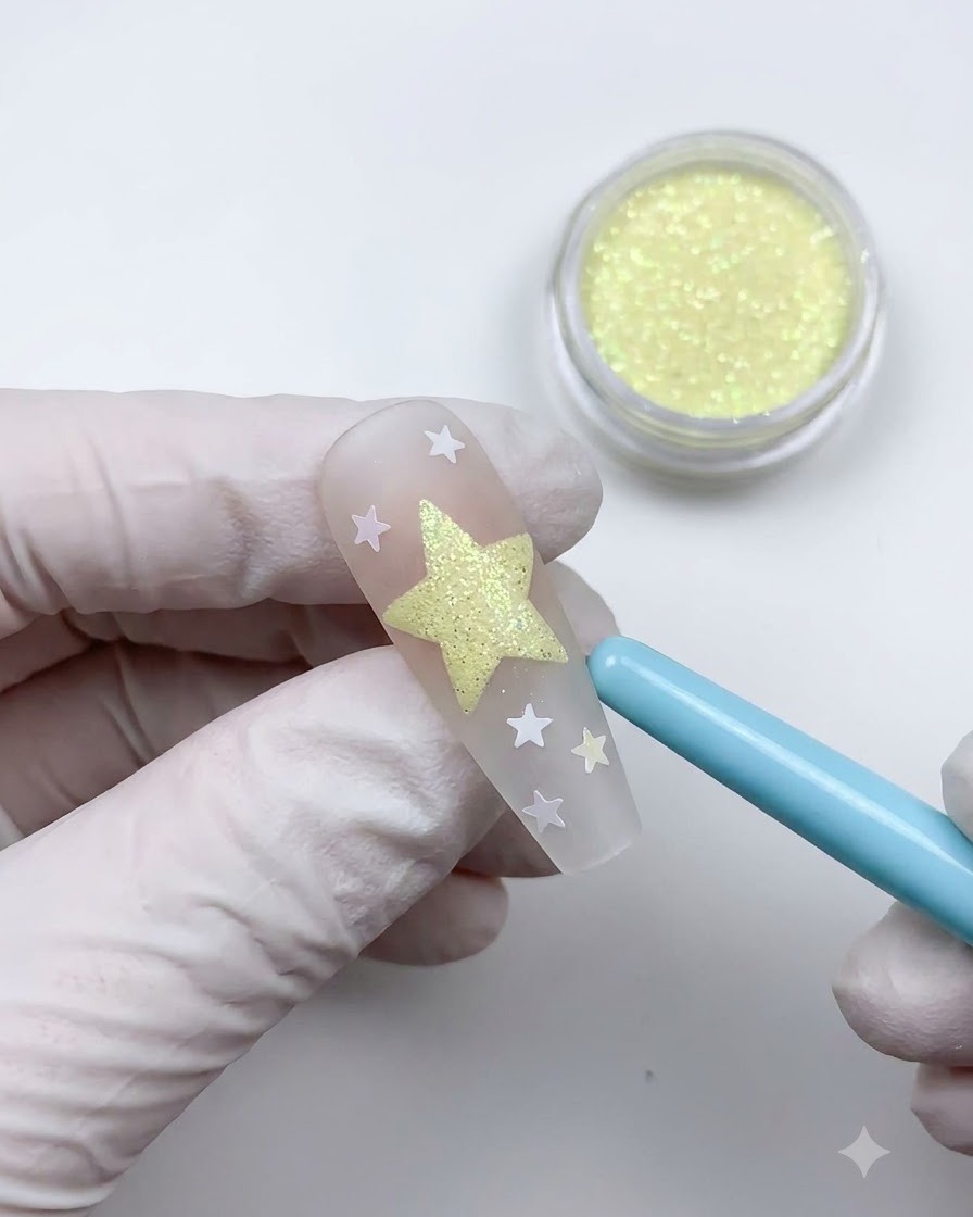 Un pennello da spolvero blu morbido che spazza via la polvere in eccesso per rivelare un design di nail art con stelle texturizzate.