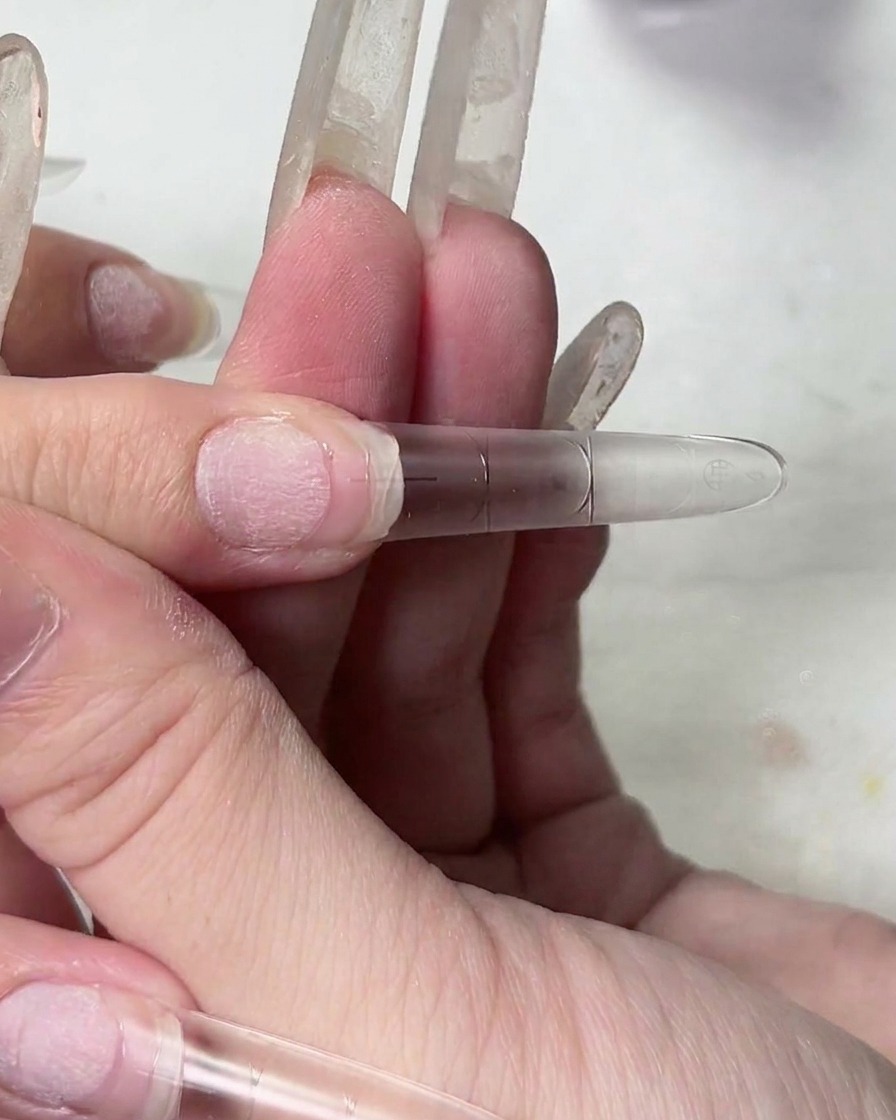 Primo piano di una mano che solleva una tip, mostrando la consistenza filamentosa del gel adesivo trasparente.