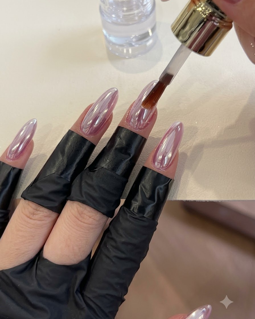 Un pennello che applica il top coat trasparente su unghie lucide con finitura chrome.