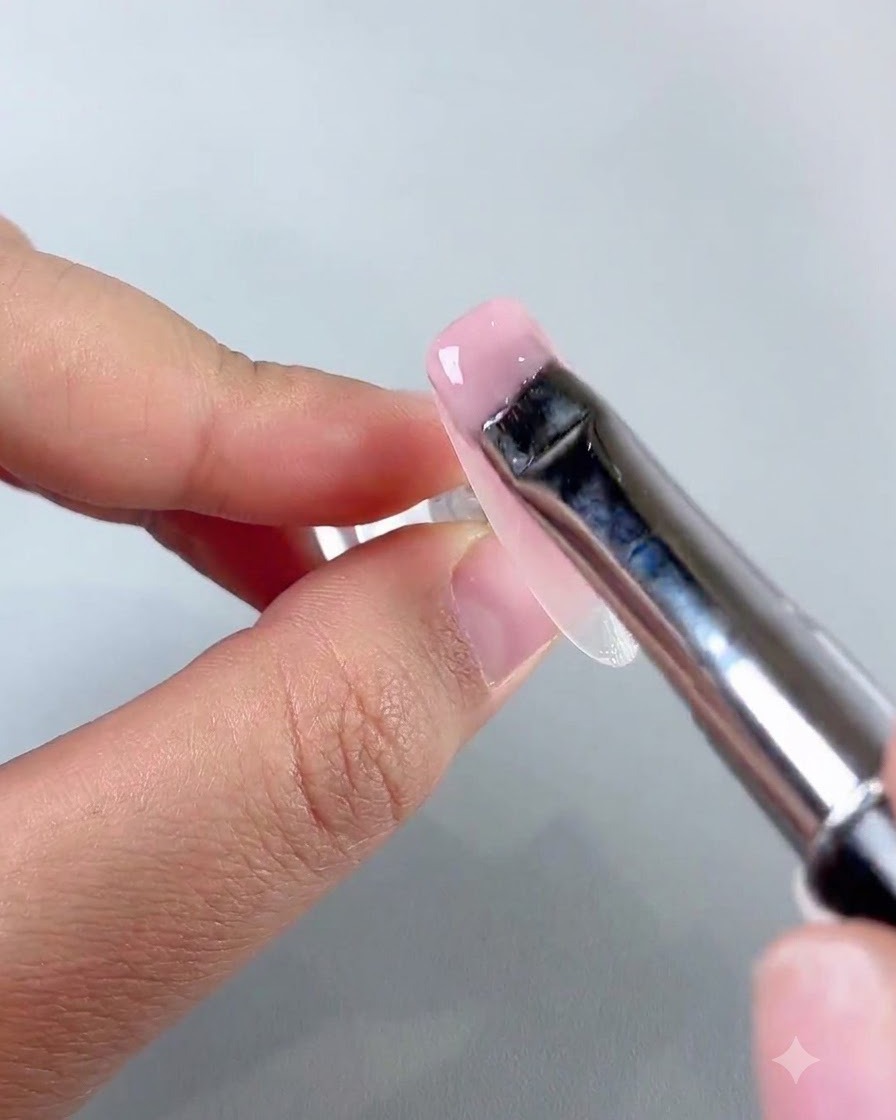 Un pennello piatto per nail art che stende uno strato uniforme di gel base jade rosa chiaro sulla superficie dellunghia.