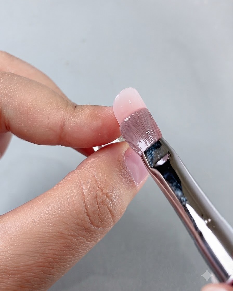 Un pennello da manicure che livella il prodotto vicino alla zona delle cuticole durante lapplicazione sullunghia.