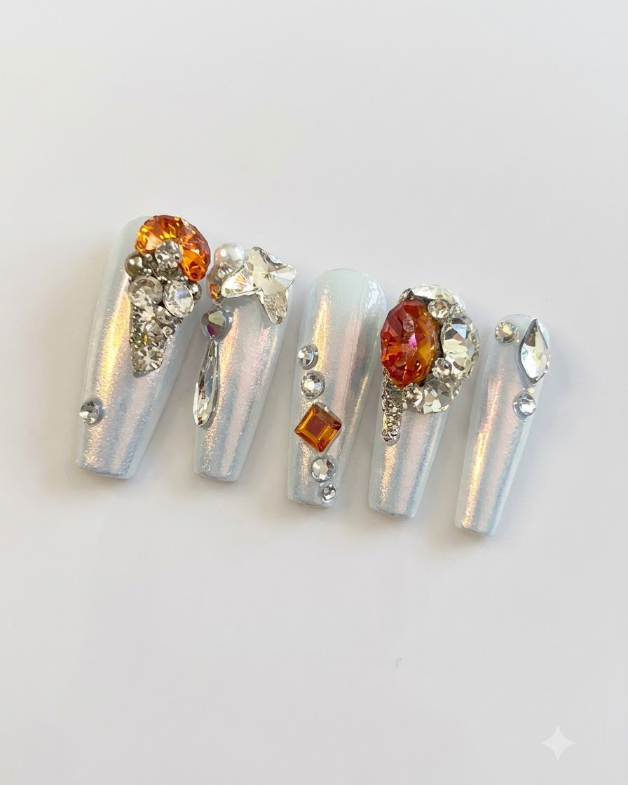 Fotografia macro ravvicinata che mostra fini perline dargento, piccoli strass e ciondoli a farfalla raggruppati sulle unghie posticce.