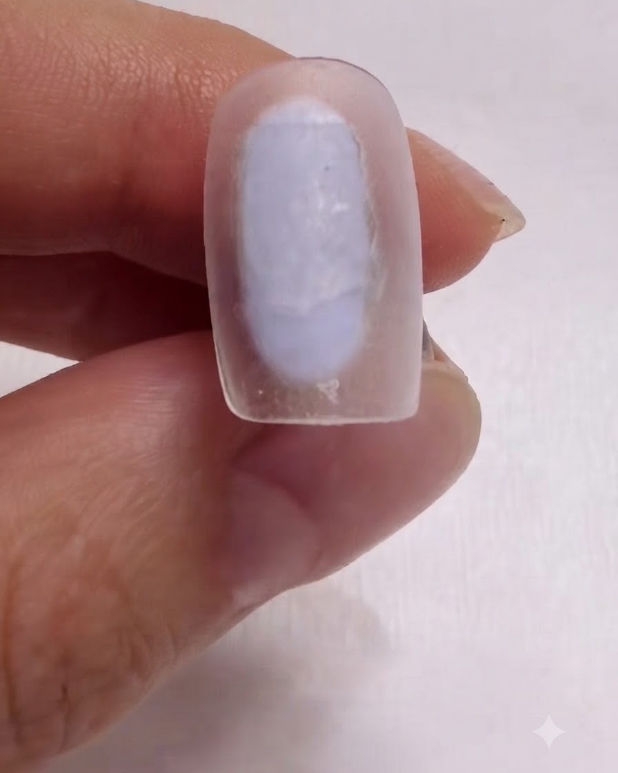 Un pennello che applica con cura una base coat bianco latte sulla superficie di ununghia.