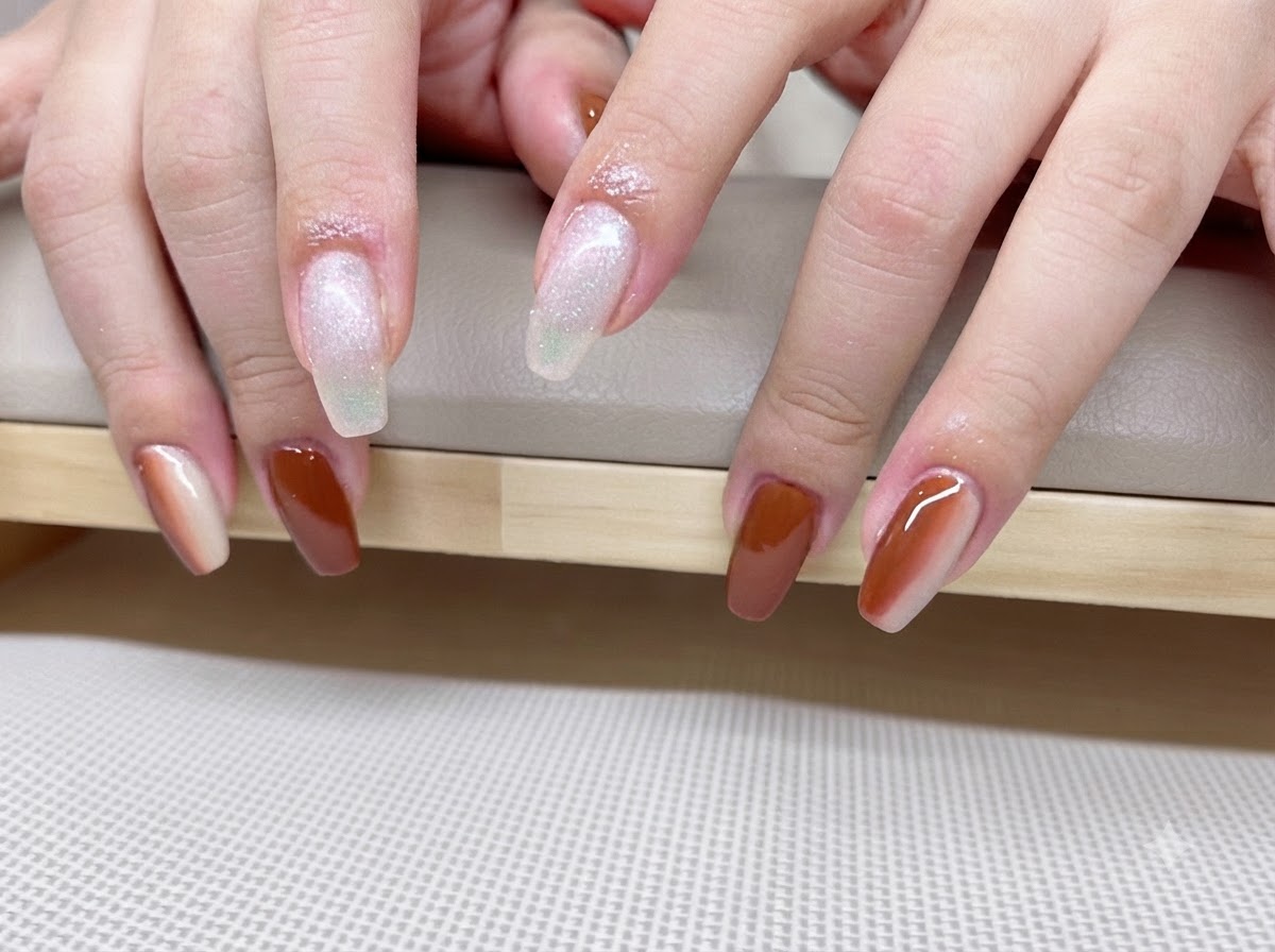 Primo piano di mani che mostrano una manicure sfumata caramello e ambra con linee luminose cat-eye.