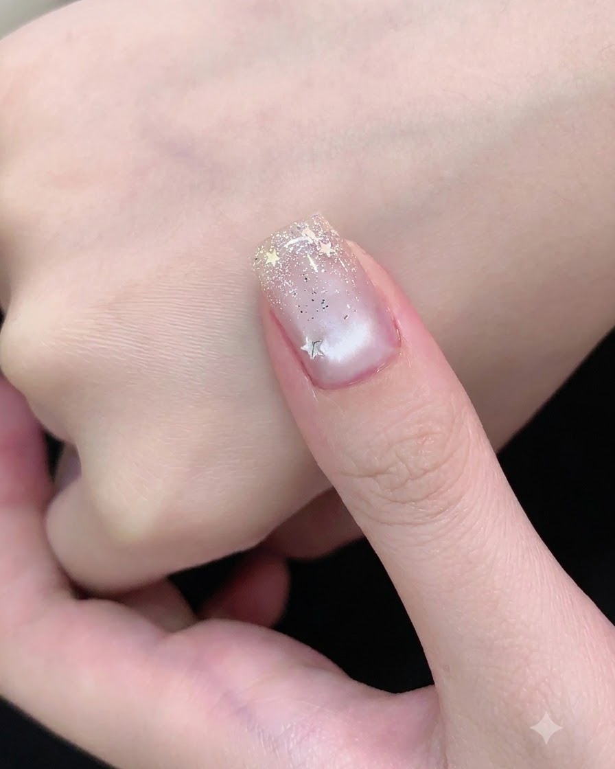 Un pennello da unghie applica il top coat trasparente sopra unghie decorate con glitter argento e stelle.