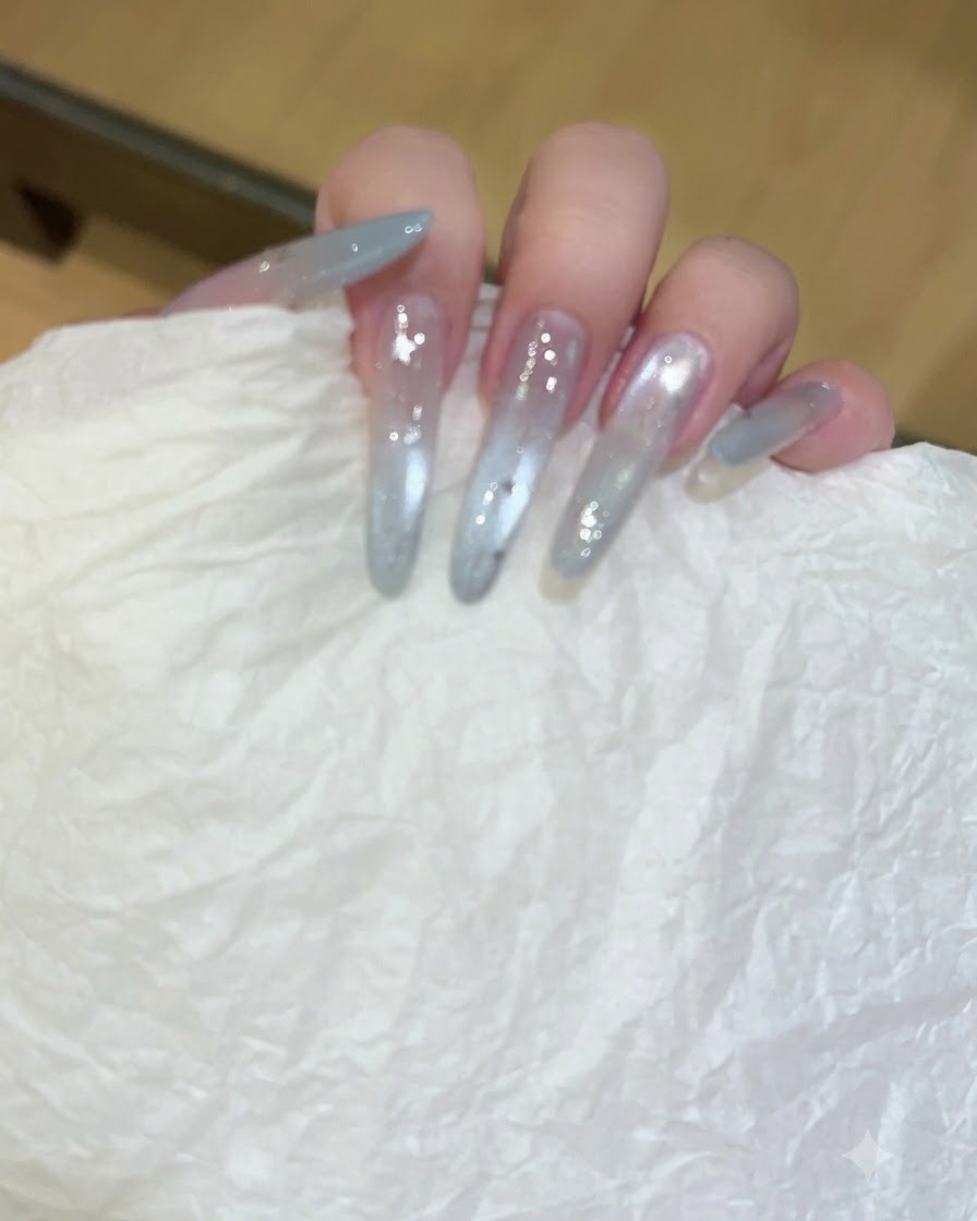 Una mano che regge un fazzoletto bianco testurizzato mentre pulisce unghie lunghe e traslucide con estensione in gel.