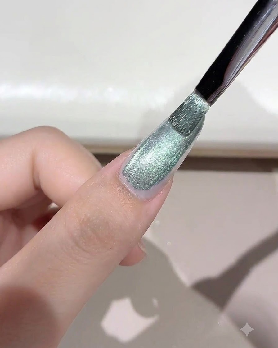 Un pennello che applica un gel cat-eye selvaggio dai toni verdi e brillanti sullunghia.