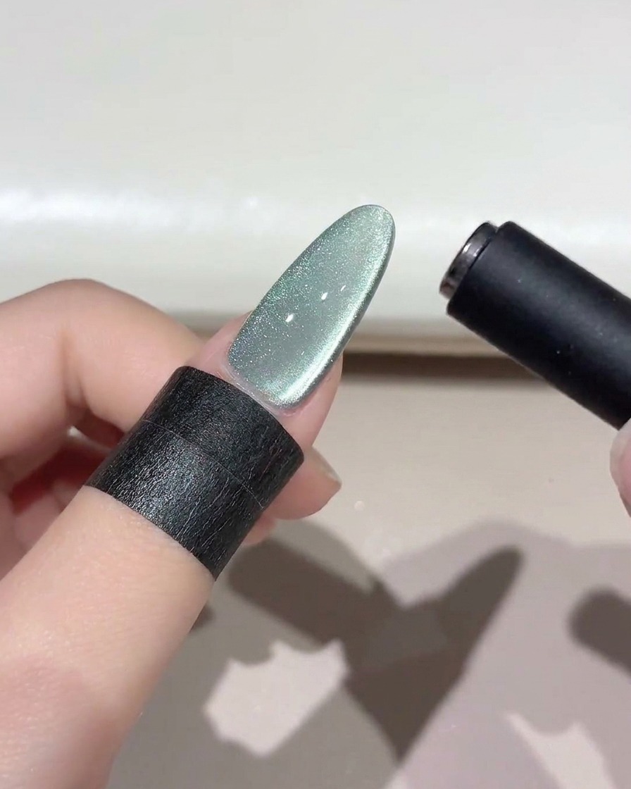 Uno strumento magnetico nero che fluttua sopra ununghia cat-eye verde brillante per modellare la fascia di luce.