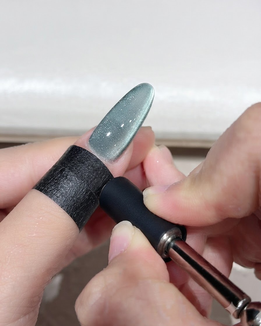 Uno strumento magnetico tenuto vicino a ununghia in gel cat-eye verde per modellare un arco di luce curvo.