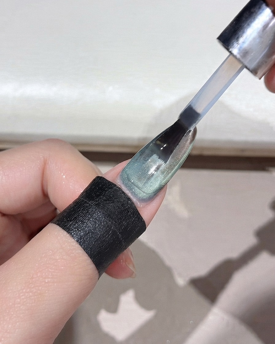 Un pennello per unghie che applica un top coat trasparente su ununghia sfumata verde con finitura a specchio.