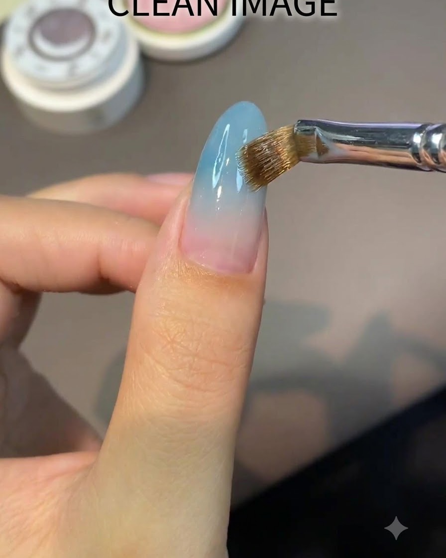 Un pennello piatto applica uniformemente un gel base nude trasparente su ununghia a mandorla.