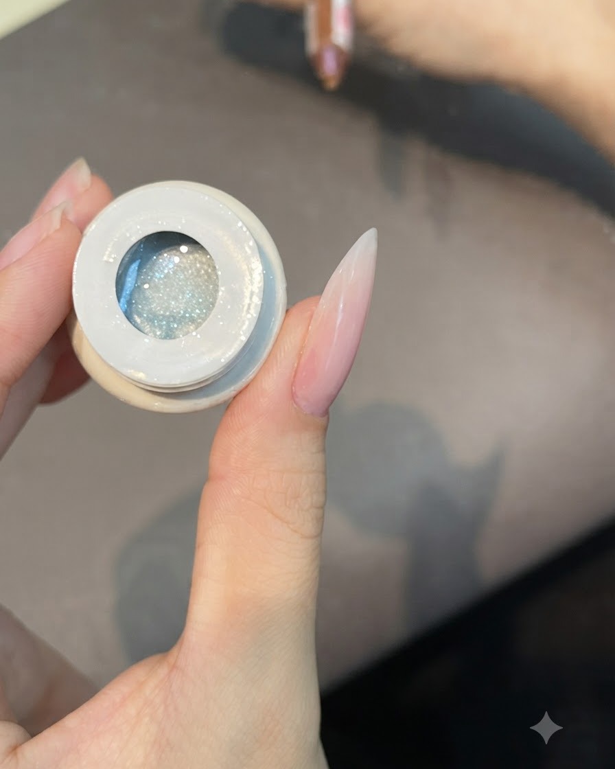 Un pennello piatto si intinge in un vasetto aperto di gel smalto cat-eye traslucido numero 49.