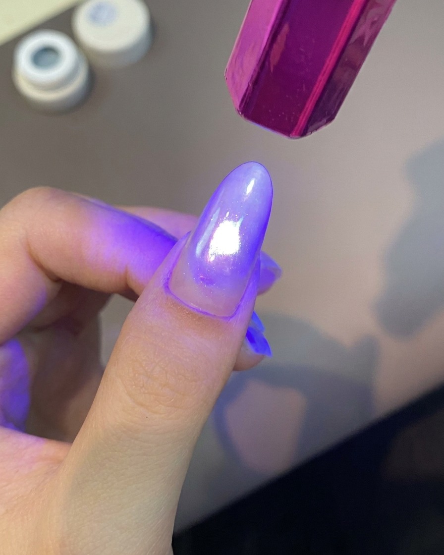 Una lampada UV portatile viola illumina con luce intensa un dito con manicure per polimerizzare il rivestimento in gel.