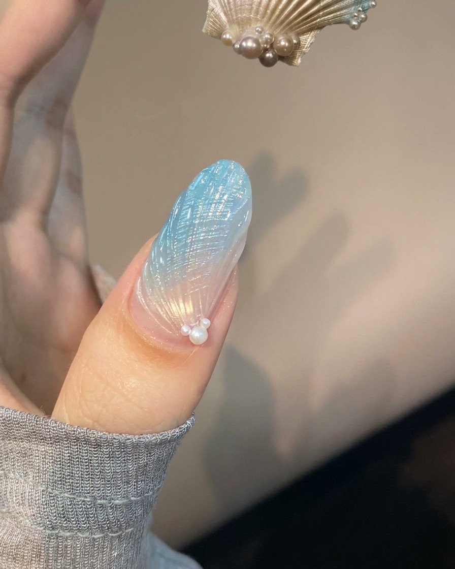 Ununghia con nail art a conchiglia blu e traslucida posizionata sotto una lampada UV viola in fase di polimerizzazione.
