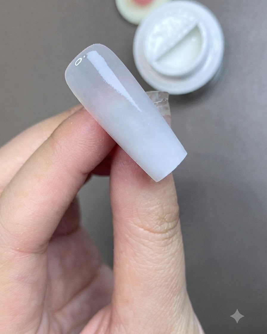 Un pennello che applica uno strato uniforme di top coat opaco su ununghia preparata color bianco latte.