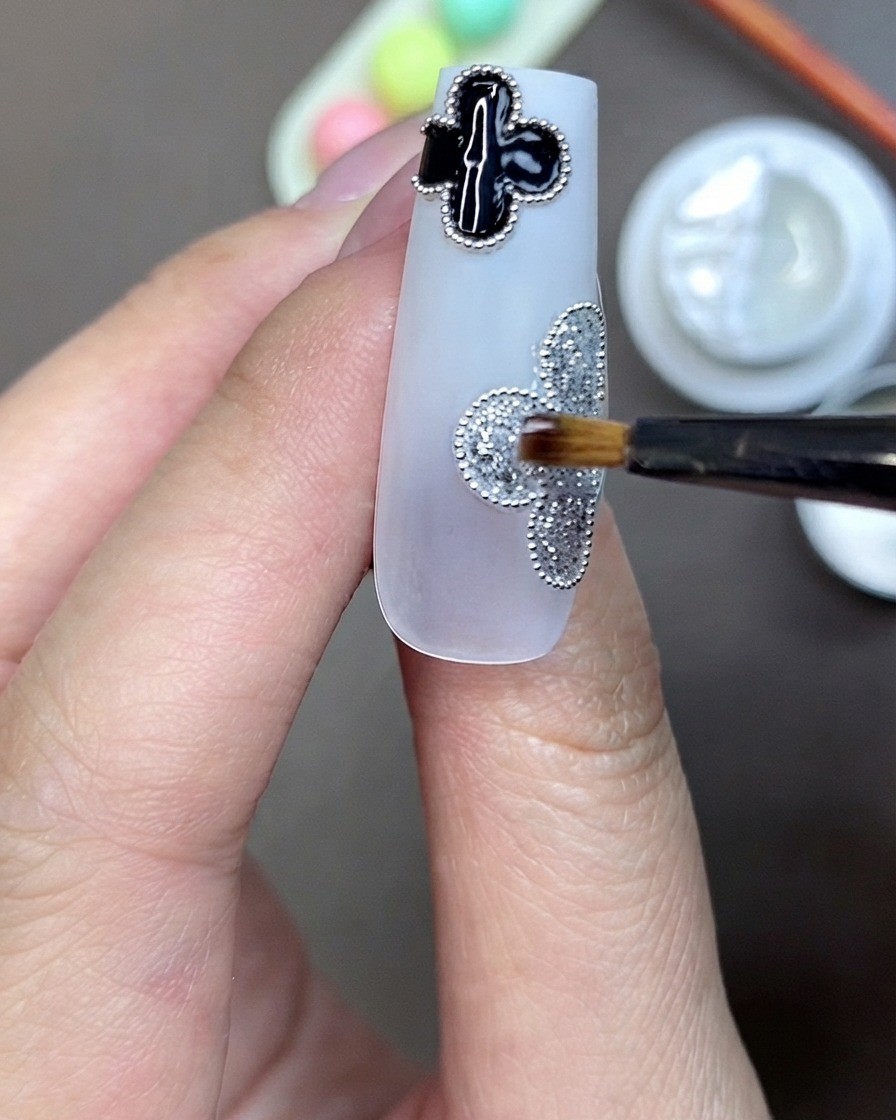 Un pennello che applica il gel adesivo trasparente per strass al centro di un motivo a trifoglio glitter argento su ununghia.