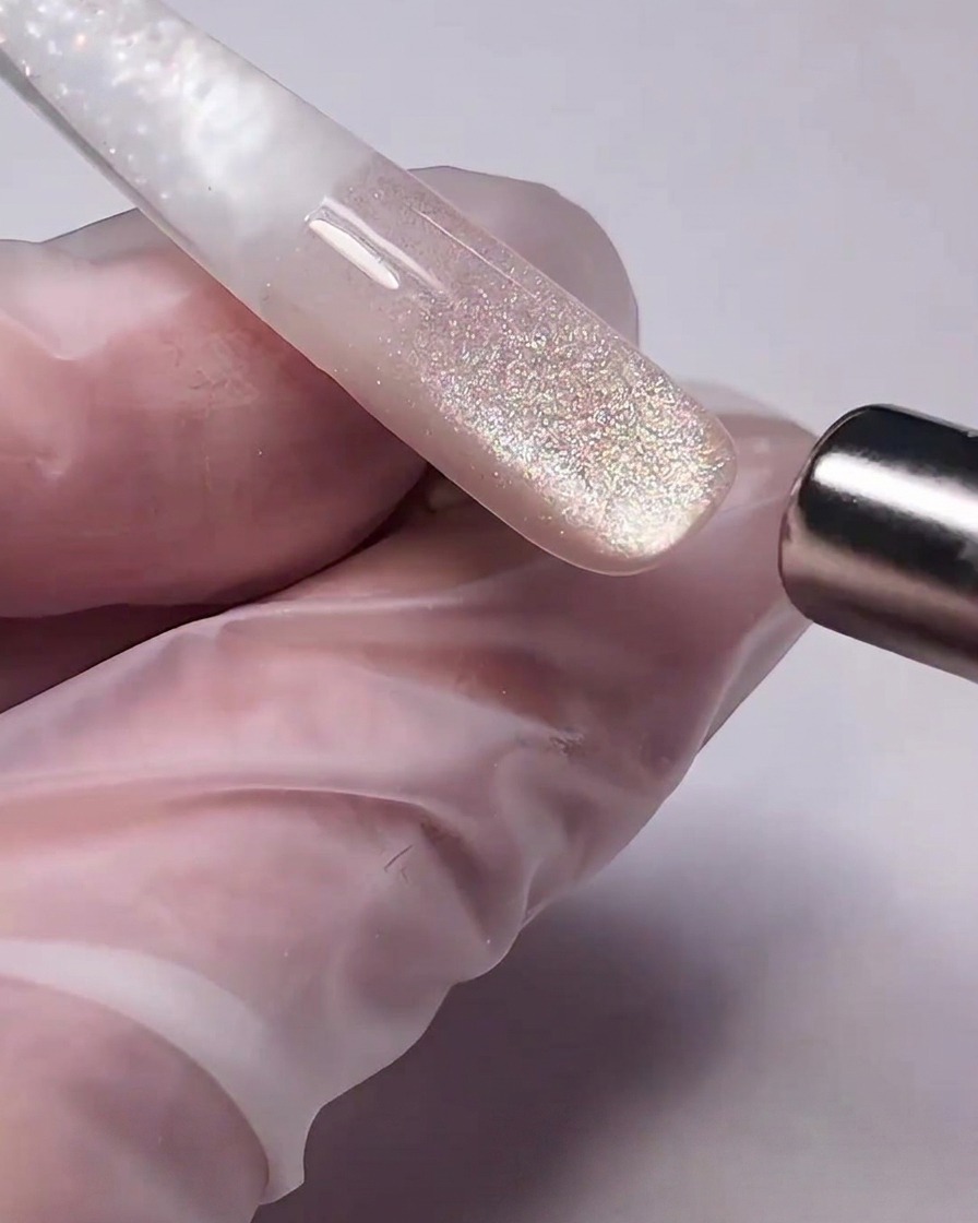 Una bacchetta magnetica cilindrica tenuta vicina al gel cat-eye bagnato su ununghia, tirando le particelle metalliche per creare un riflesso.