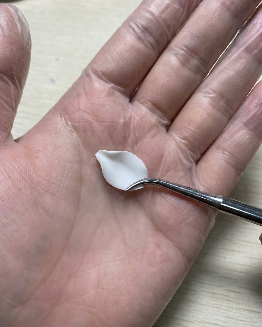 Una mano guantata che tiene uno strumento in silicone per intaglio mentre leviga un petalo di gel bianco 3D adagiato su un tappetino in silicone.