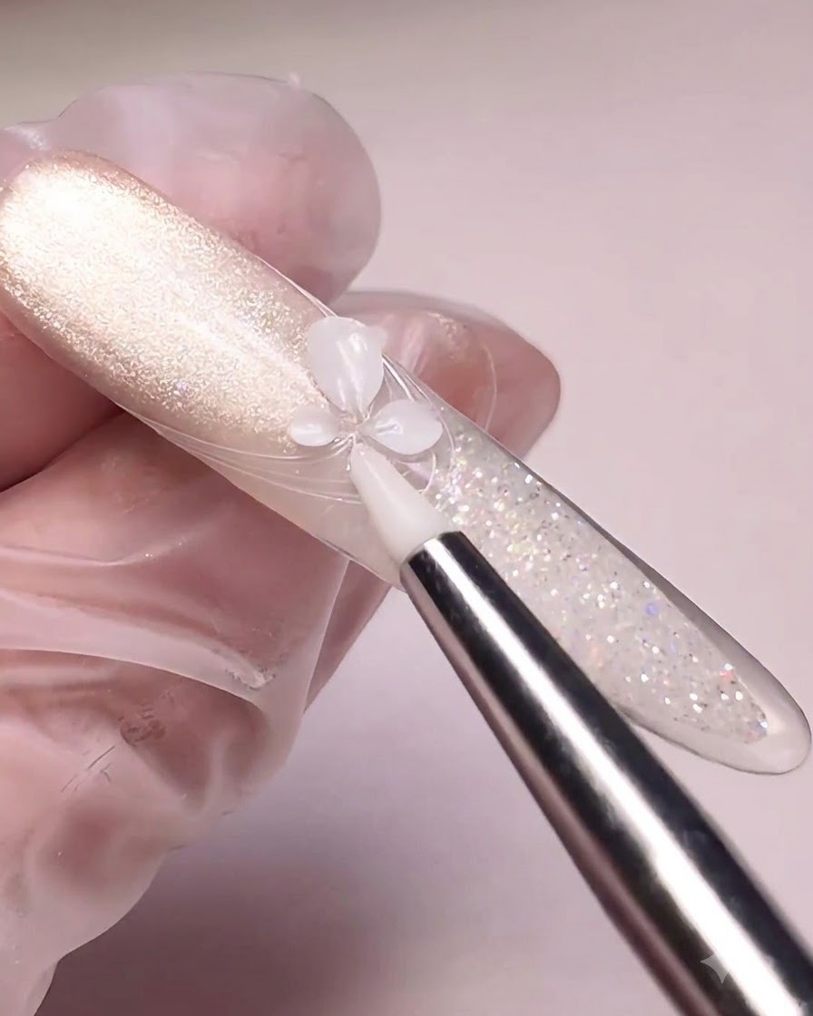 Uno strumento in silicone che preme il gel da intaglio bianco per formare petalli di fiori su una tip dipinta con effetto cat-eye.