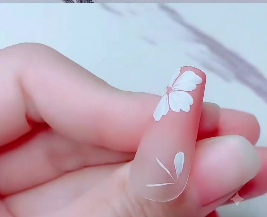 Primo piano di ununghia che mostra petali parziali di fiori di ciliegio bianchi dipinti vicino al bordo inferiore.
