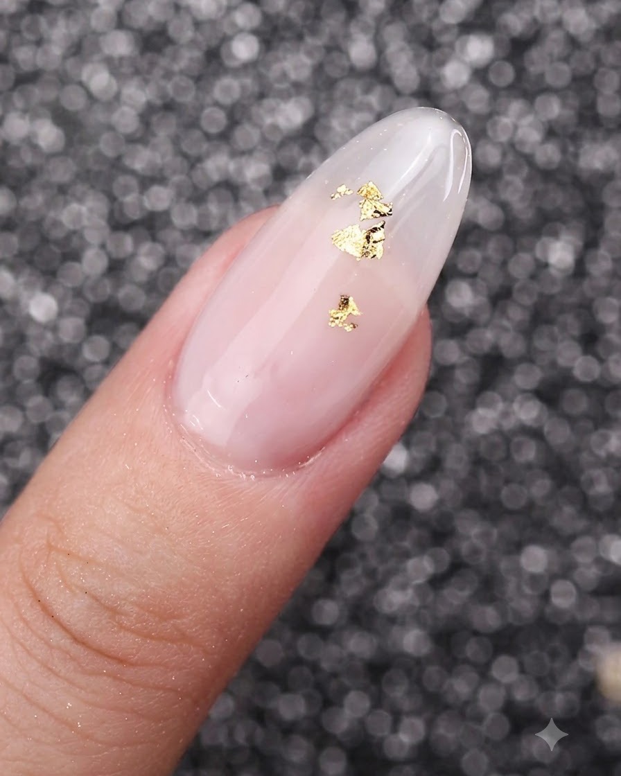 Una vista ravvicinata di fiocchi di foglia oro posizionati delicatamente sopra ununghia con manicure in gel bianco latte.
