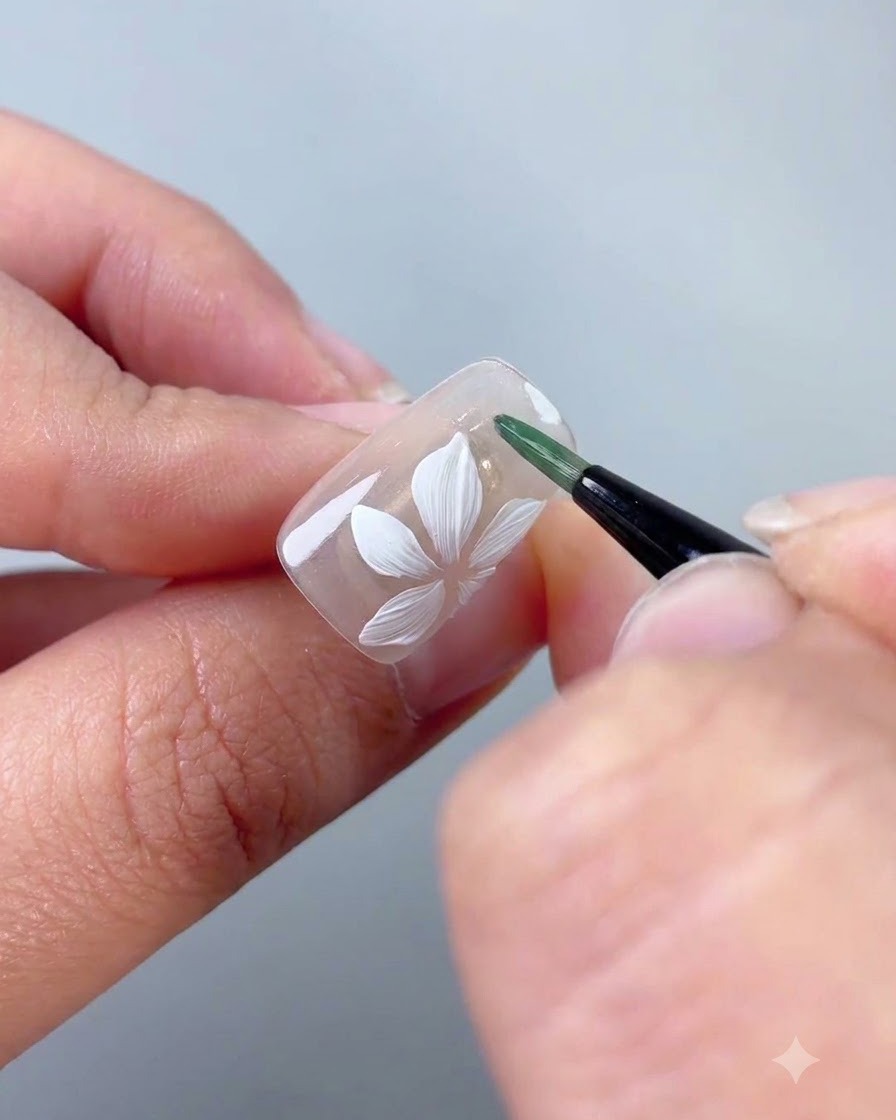 Un pennello liner che applica gel verde per formare una sottile foglia accanto al fiore bianco.