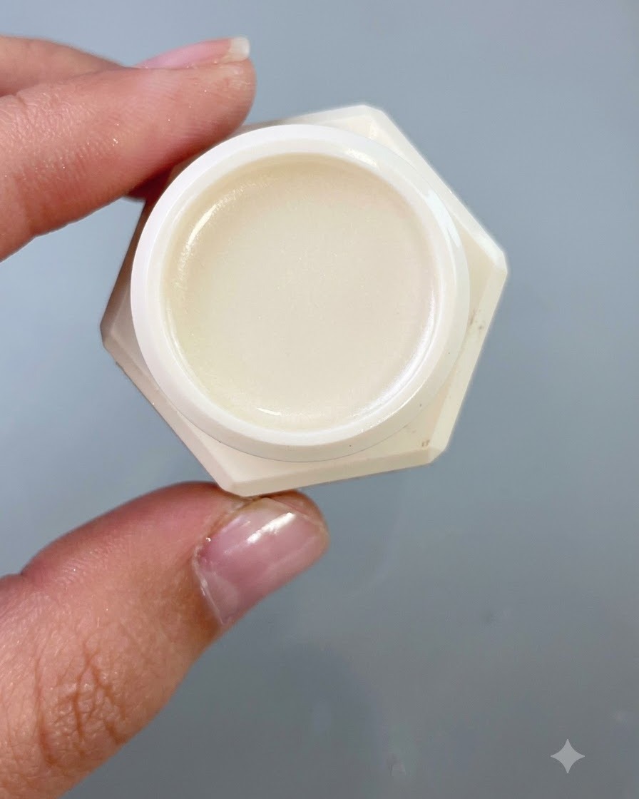 Un primo piano di un piccolo barattolo contenente gel di trasferimento, tenuto contro uno sfondo grigio neutro.