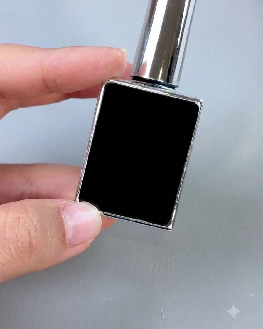 Un piccolo flacone cosmetico nero con tappo argentato e pennello applicatore, esposto in verticale su uno sfondo grigio.