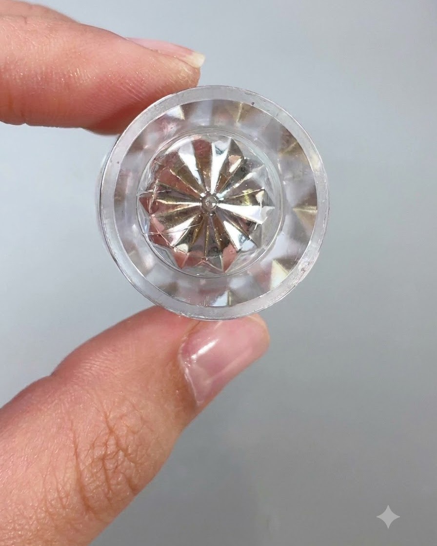 Una vista ravvicinata della parte superiore di un contenitore di cristallo trasparente e sfaccettato o di uno strumento applicatore che riflette la luce su uno sfondo chiaro.
