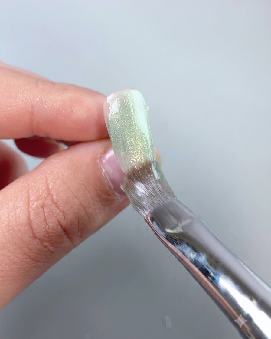 Un pennello per unghie che livella uno strato di gel cat-eye verde trasparente su una superficie di un unghia press-on.