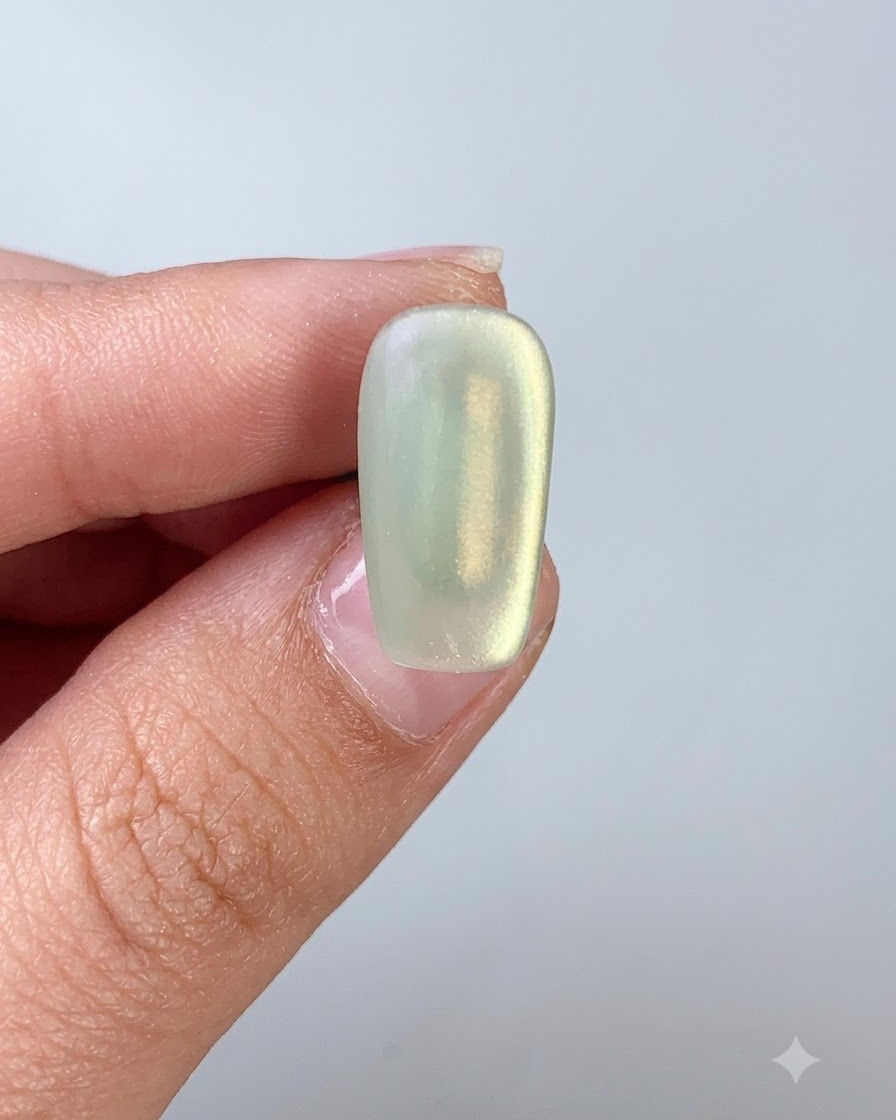 Un pennello per unghie che applica il top coat sopra ununghia in gel cat eye verde.
