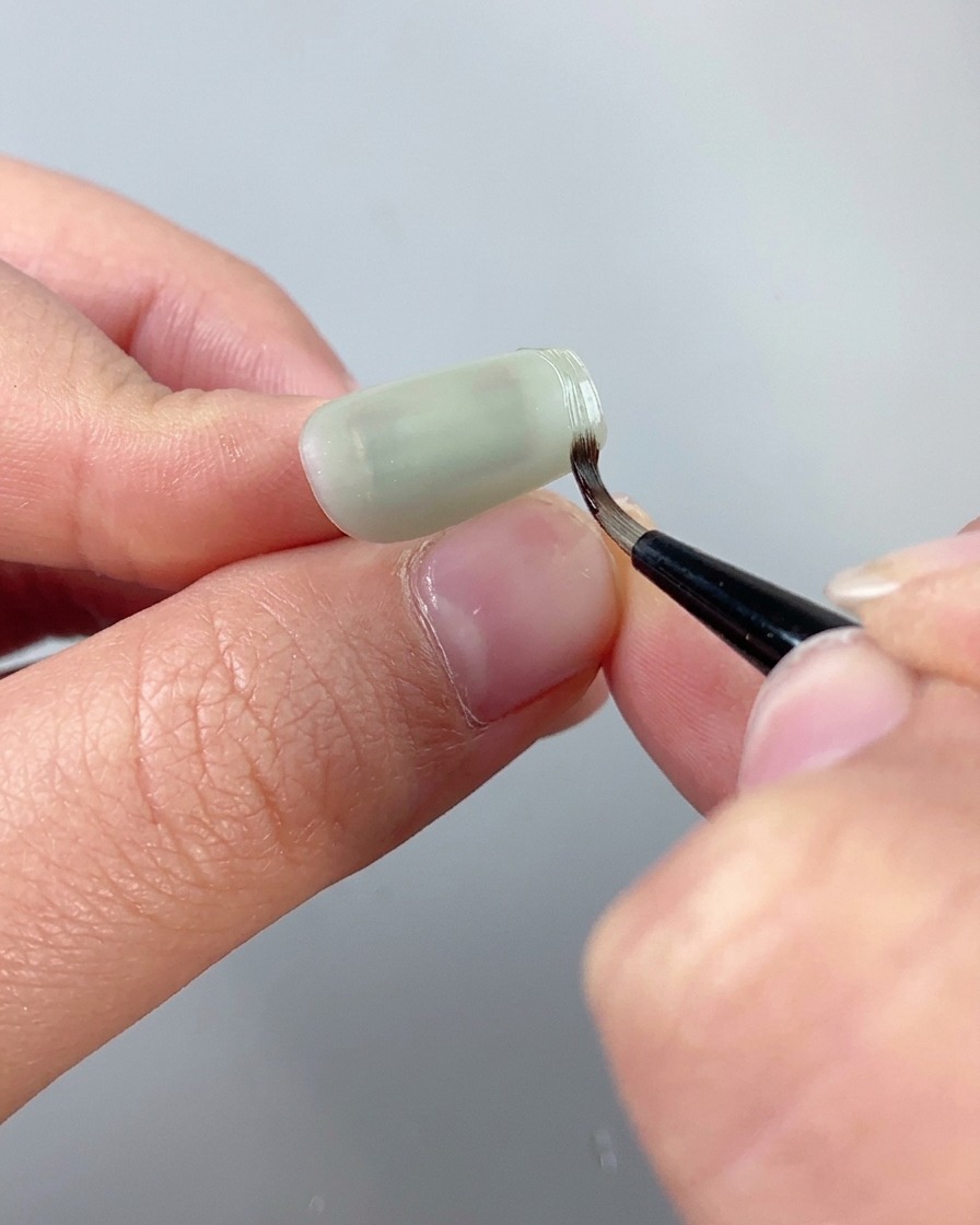 Un pennello per dettagli fini che usa il gel per scultura texturizzato trasparente per tracciare un bordo rialzato lungo il contorno di ununghia cat eye.