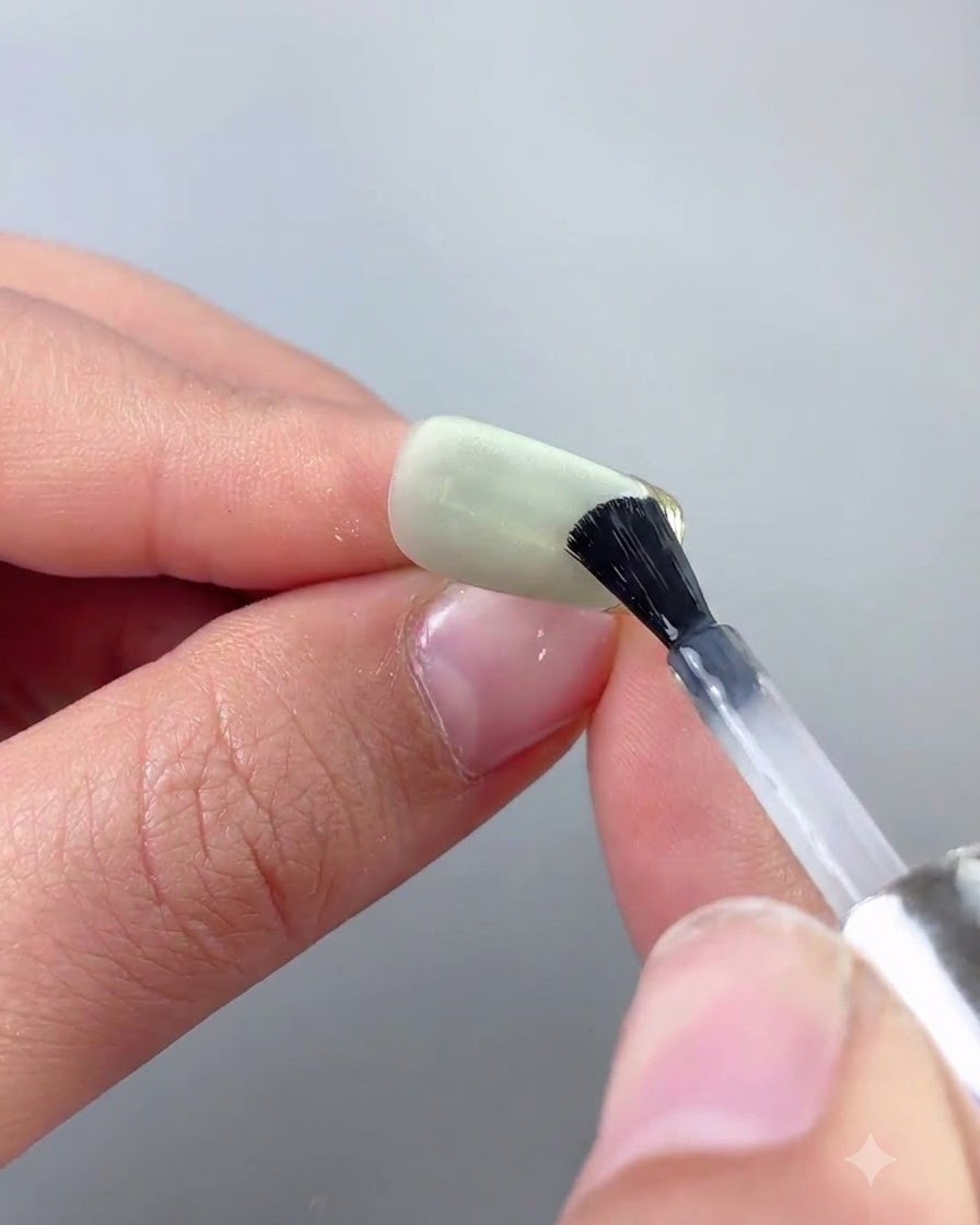 Un pennello fine per nail art che applica con precisione il top coat lungo il bordo in cromo oro di ununghia cat eye verde.