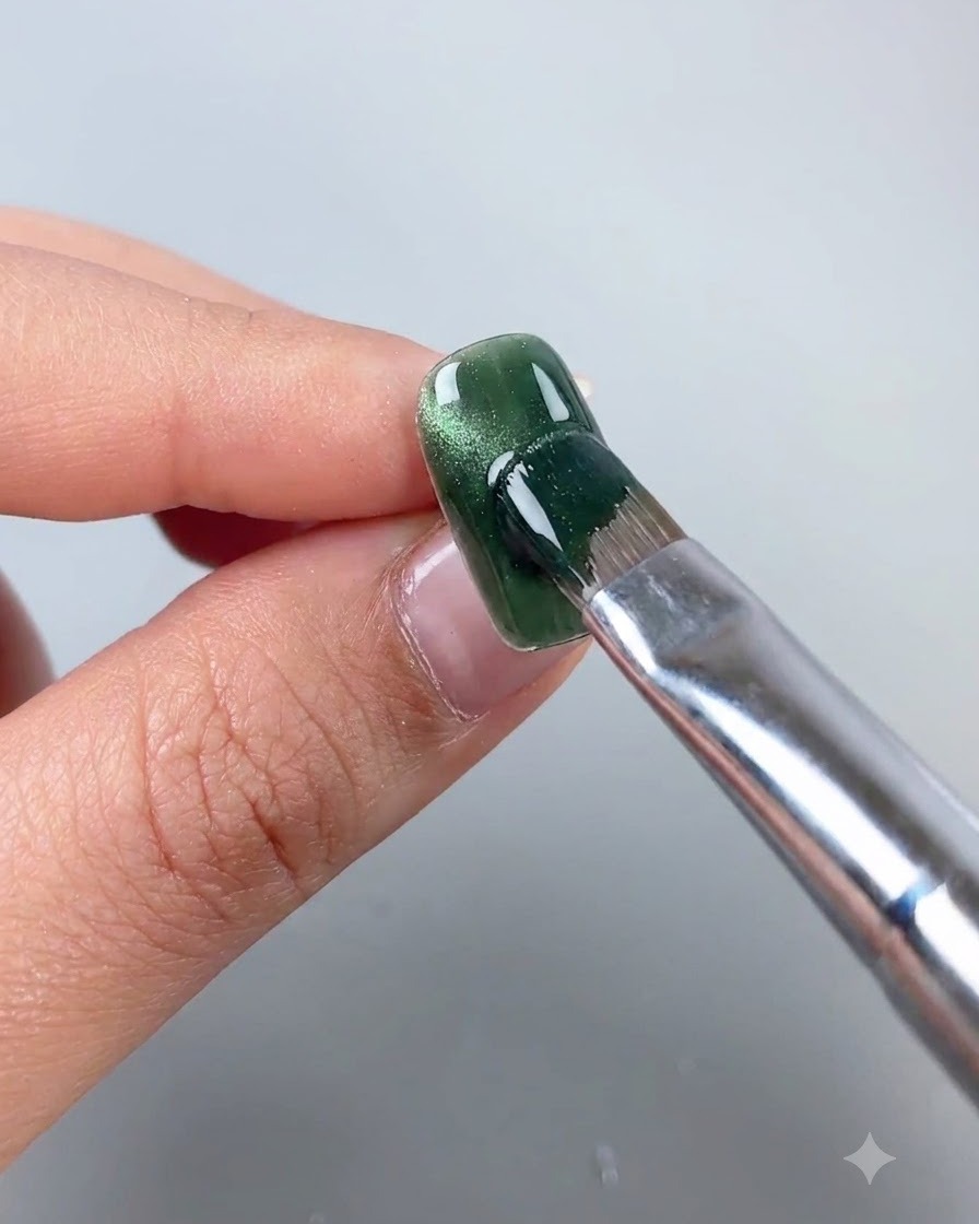Una bacchetta magnetica tenuta vicino a ununghia in gel cat eye verde per spostare le particelle magnetiche in una linea ad arco laterale.