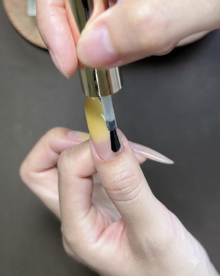 Un pennello che applica lo smalto gel cat-eye sopra lunghia del pollice con sfumatura gialla.