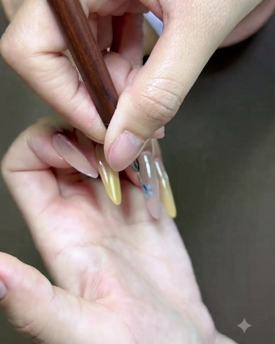 Un primo piano dettagliato di un pennello fine per nail art che aggiunge un accento floreale rosa sullunghia.