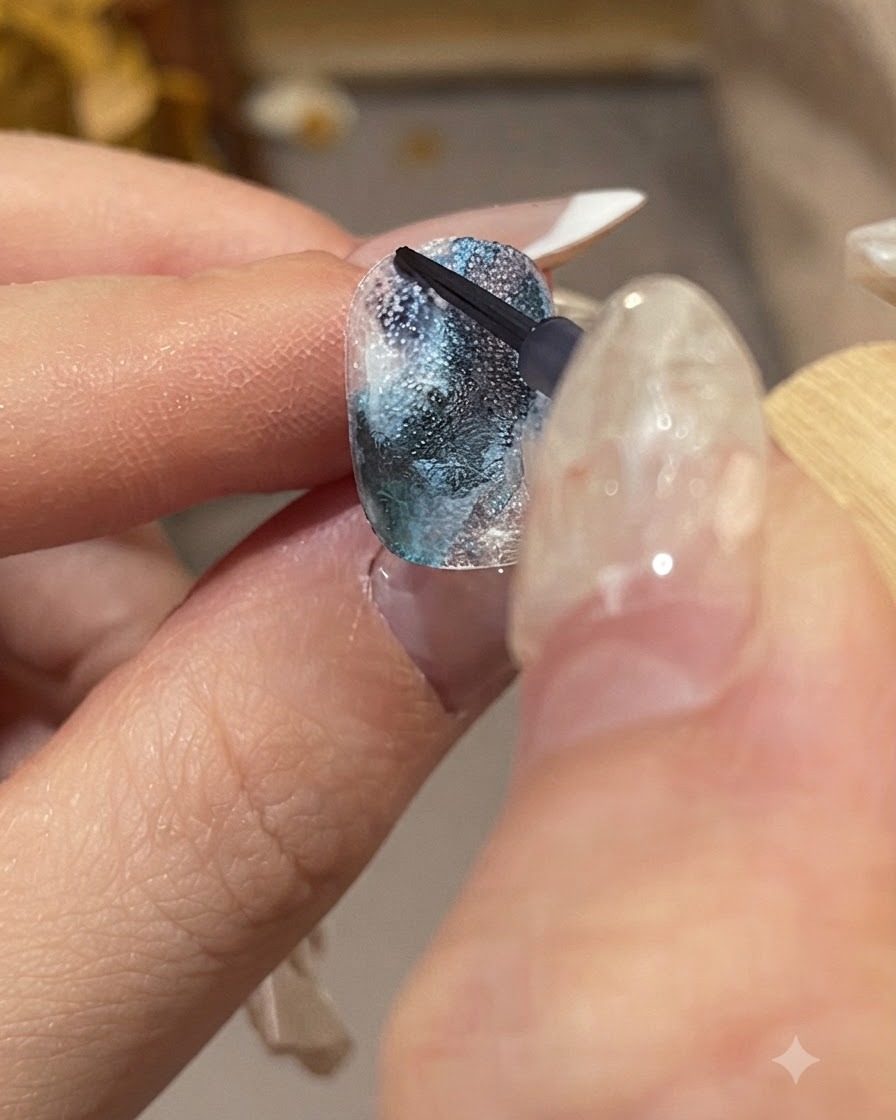 Primo piano dettagliato di una mano curata che tiene un pennello fine per applicare gocce di inchiostro blu scuro su una superficie ungueale strutturata.