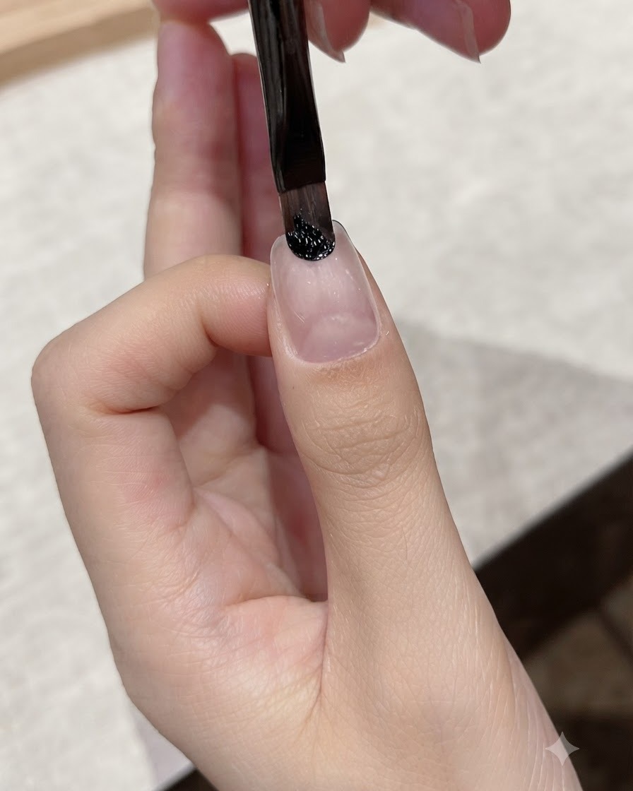 Un pennello a punta fine applica del gel nero scuro vicino alla zona delle cuticole di ununghia naturale.