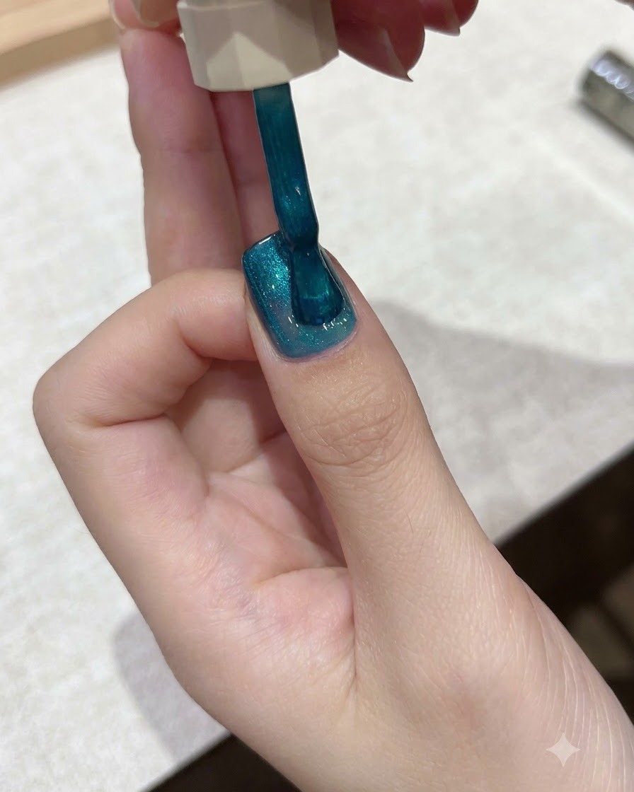Un pennello applica lo smalto semipermanente cat-eye blu ottanio vibrante sulla superficie di ununghia.