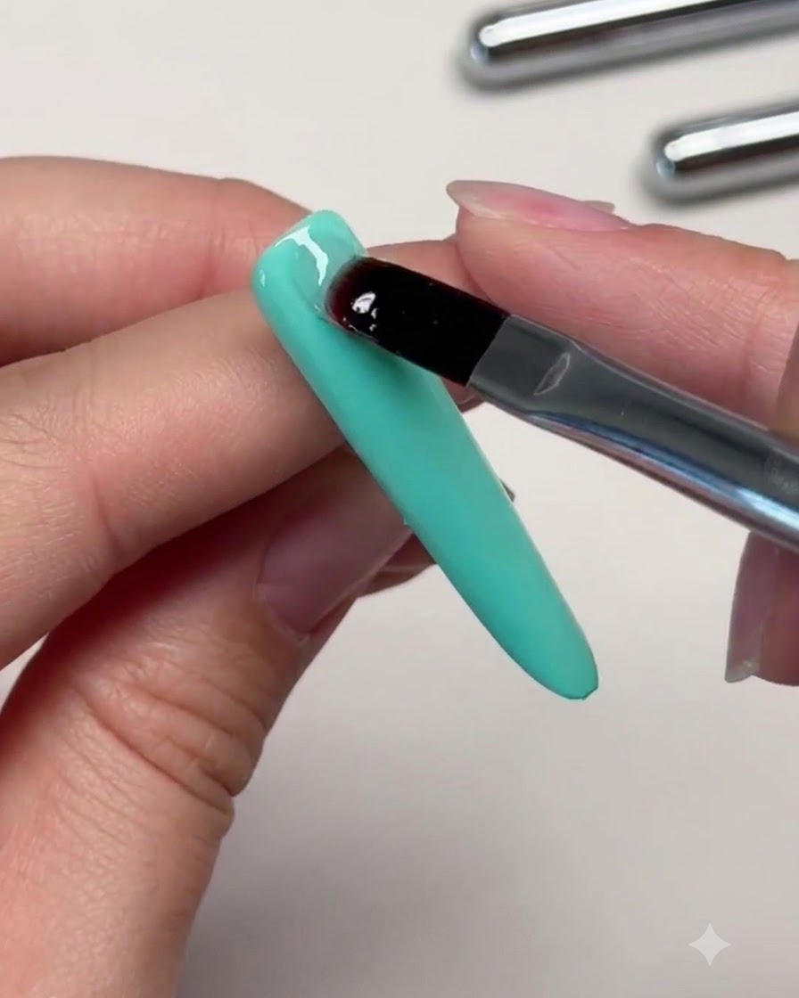 Un pennello che posiziona una pallina di gel trasparente costruttore sulla parte superiore di ununghia verde menta per creare lapice.
