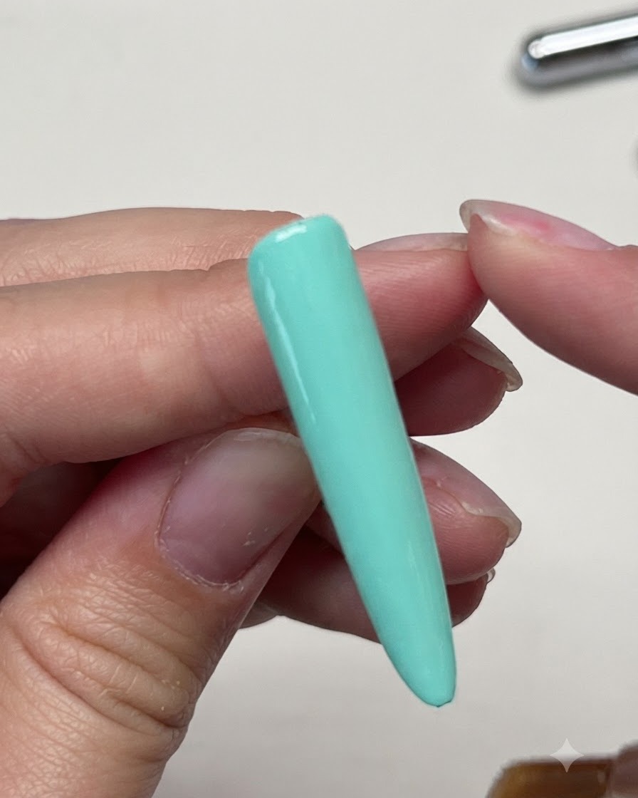 Un pennello che stende un top coat opaco sullunghia ricostruita verde menta a tinta unita.