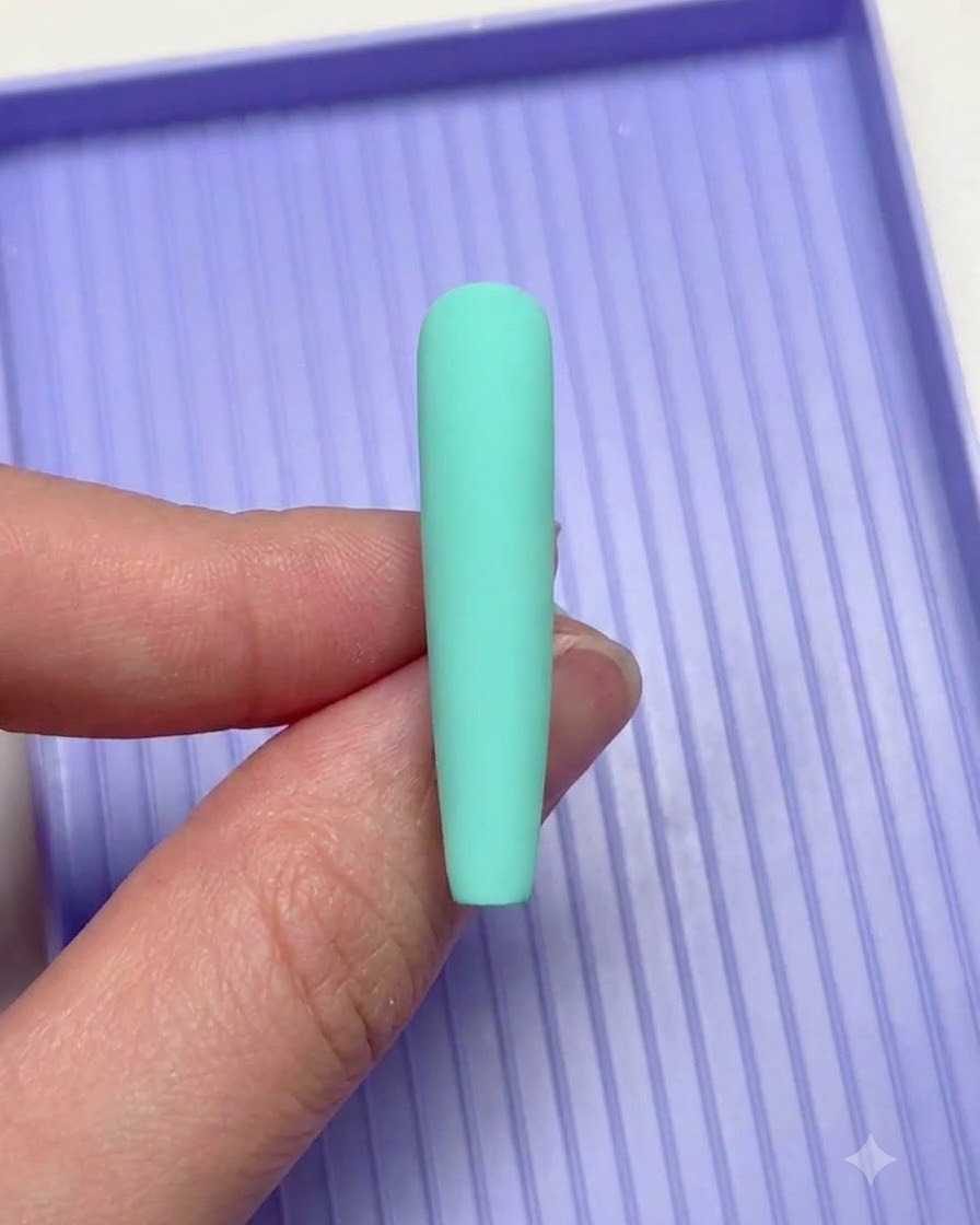 Una mano che tiene ununghia verde menta sopra un vassoietto viola durante la nail art.